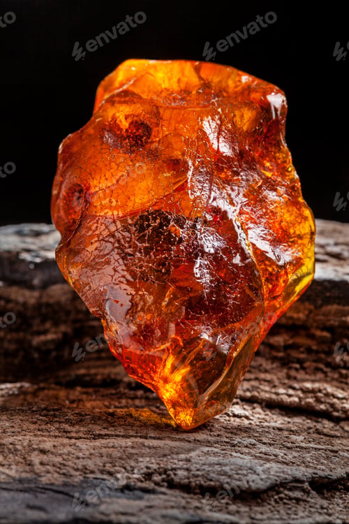 Preview: Natural amber. A piece of yellow and red semi transparent natural amber on piece of stoned wood