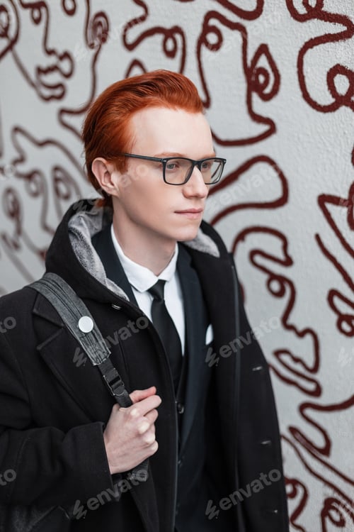 Preview: handsome red-haired hipster guy with glasses in fashionable clothes with a coat