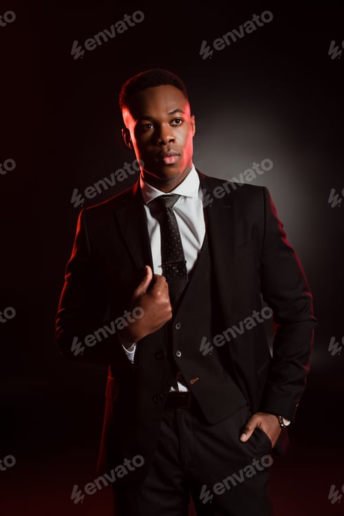 Preview: stylish african american man in formal wear standing with hand in pocket on black
