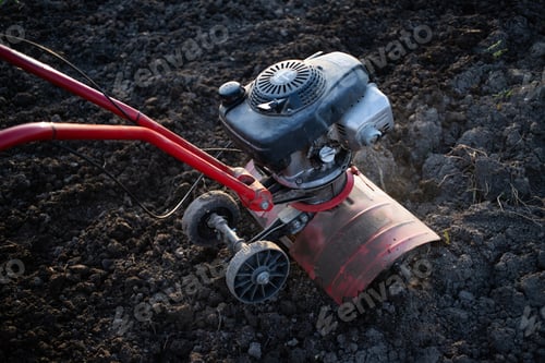 Preview: organic farming man ploughs the ground at sunset with a tiller preparing the soil for sowing