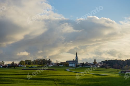 Preview: A serene rural landscape with a church steeple and scattered houses under a dramatic cloudy sky