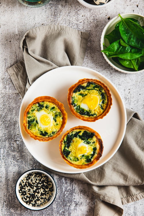 Preview: Eggs, spinach and cheese baked in tartlets on a plate on the table top and vertical view