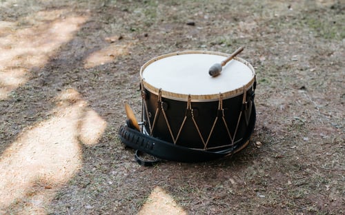 Preview: Medieval drum with drumstick lying on grass outdoors