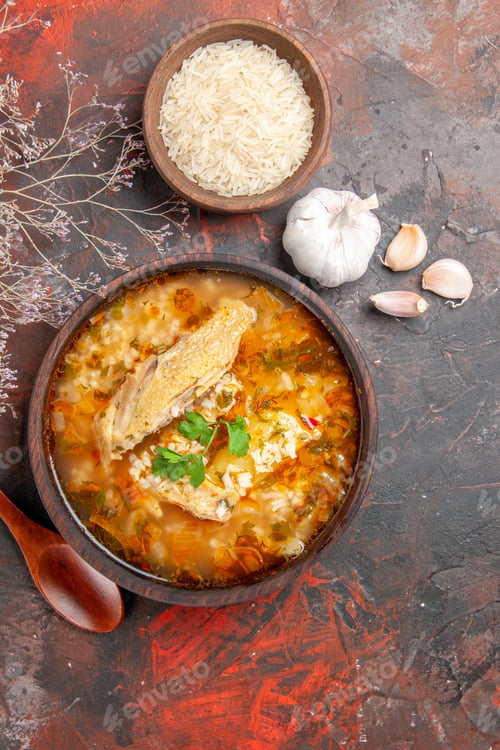 Preview: top view homemade chicken and rice soup in wooden bowl wooden spoon bowl of rice garlic on dark red