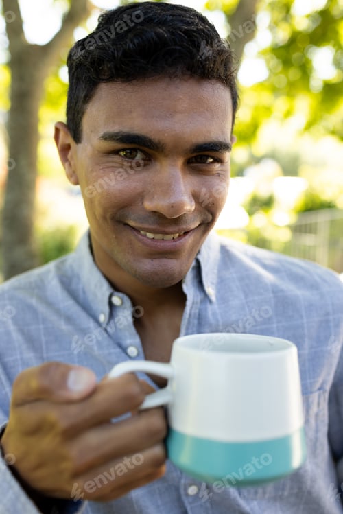 Preview: Portrait of happy biracial man holding mug on balcony at home