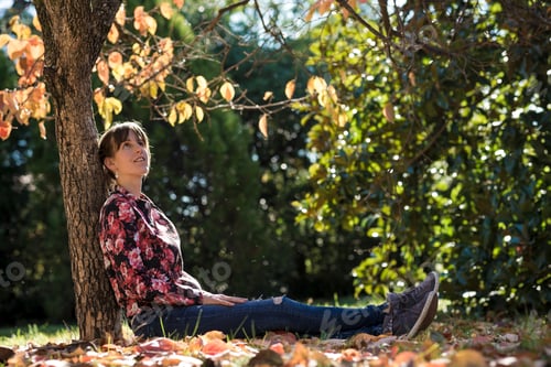 Preview: Young brunette sitting under an autumn tree