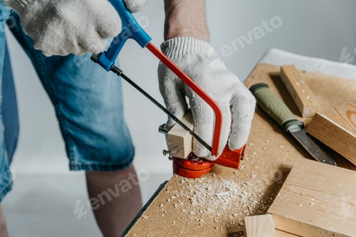 Preview: A man in work gloves is sawing a small block of wood with a hand saw. Handmade. DIY.