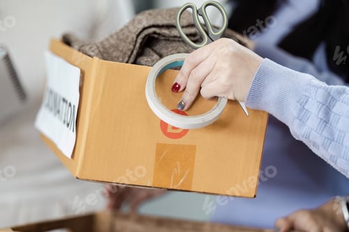 Preview: Individual preparing a donation box with clothing items.