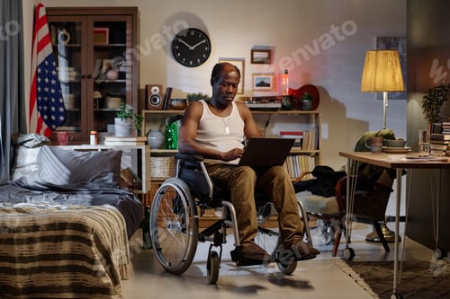 Preview: Black Man in Wheelchair Looking Through Information on Laptop Screen