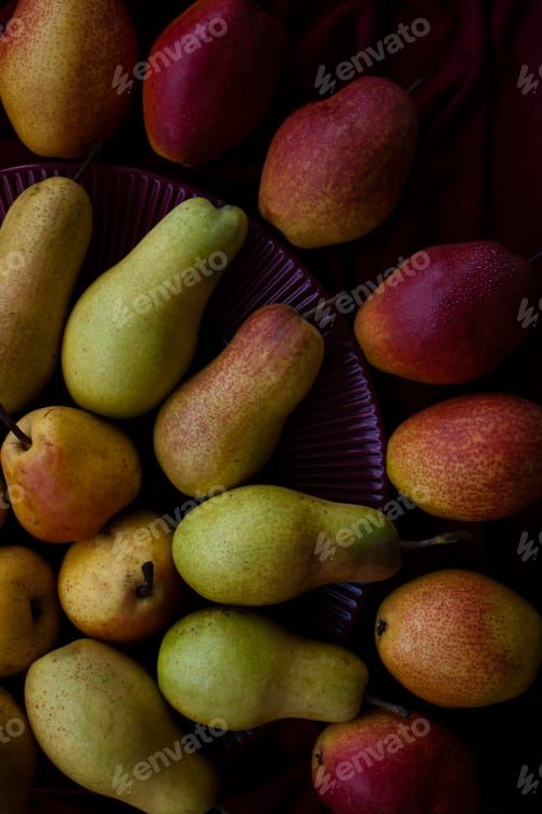 Preview: Yellow and red juicy fragrant pears lie on a cherry plate on a dark cherry tablecloth.