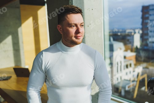 Preview: A young handsome man in a white sweater is standing in a spacious bright office