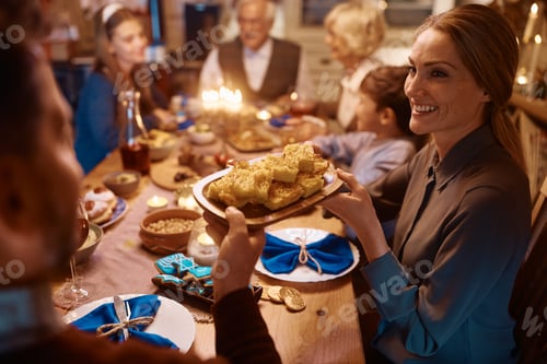 Preview: Happy woman passing food to her husband during family dinner on Hanukkah.