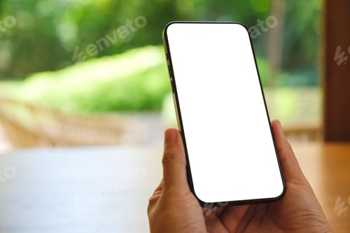 Preview: Mockup image of a woman holding and using mobile phone with blank desktop at home