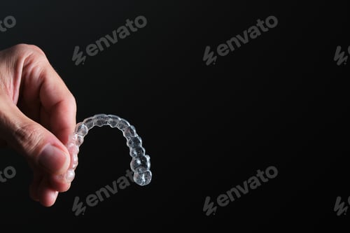 Preview: man hand holding transparent dental retainer on black background