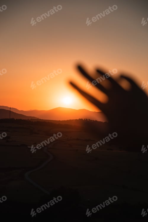 Preview: defocused hand blocking the sun on a warm summer sunset in the mountains