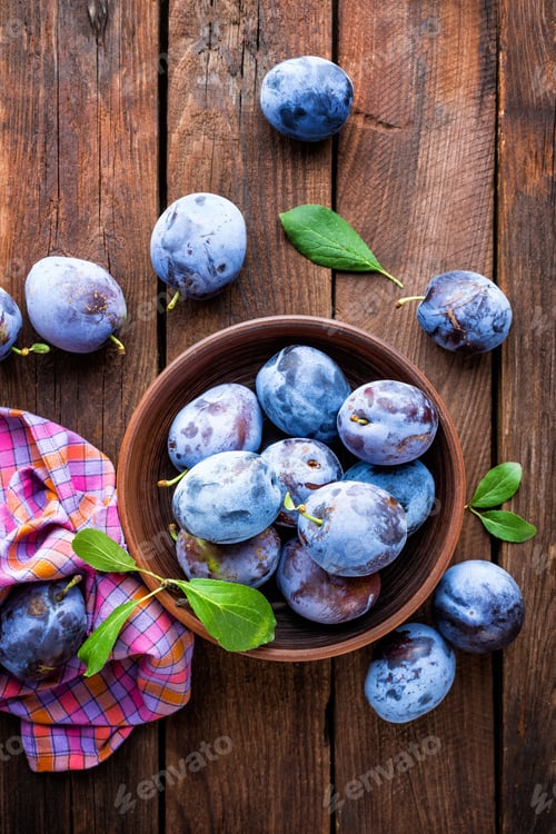 Preview: Fresh plums with green leaves on wooden rustic background, top view