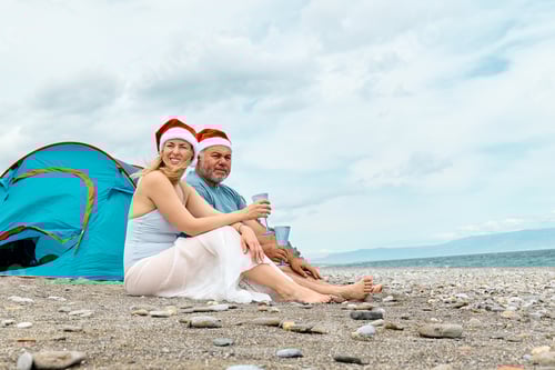 Preview: Middle aged couple wearing santa hats having christmas picnic on the beach.