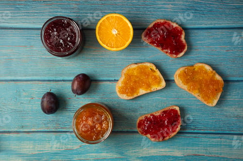 Preview: Orange and plum confiture in a glass jar and on the toast breads, top view