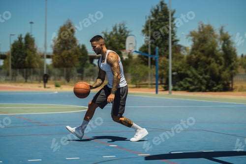 Preview: Sporty caucasian guy with cool tattoos playing basketball on the outdoor court