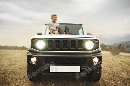 Preview: Little boy sitting on a hood of an off-road car parked in mountains