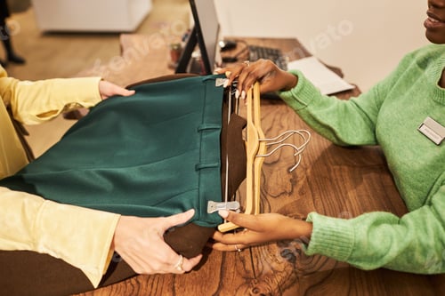 Preview: Woman handing clothing items to shop assistant for purchase in boutique