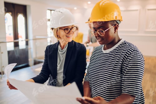 Preview: Portrait of two multiracial architect looking at blueprints in an office