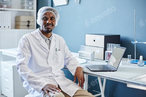 Preview: Portrait of Smiling African American Male Lab Chemist Sitting At Table In Laboratory