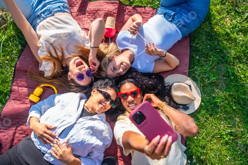 Preview: Four diverse young women taking a selfie lying on a blanket in a park