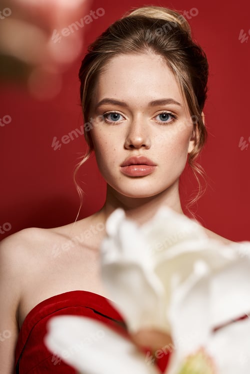 Preview: Young beautiful woman in elegant red attire against a vibrant background with white flowers