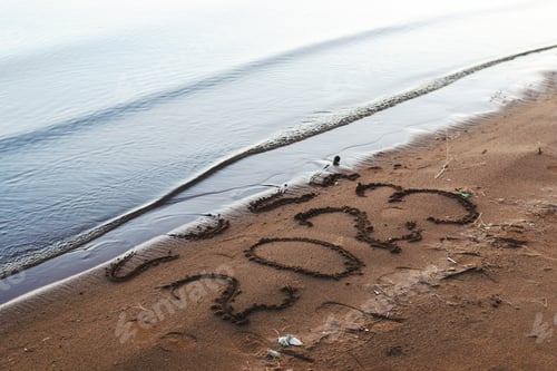 Preview: A side view of the years 2022 and 2023 drawn in the sand as the water washes away.