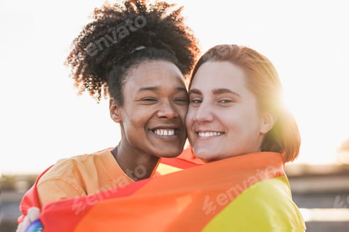 Preview: Mulitracial lesbian couple hugging together outdoor with sunset in background - LGBTQIA concept