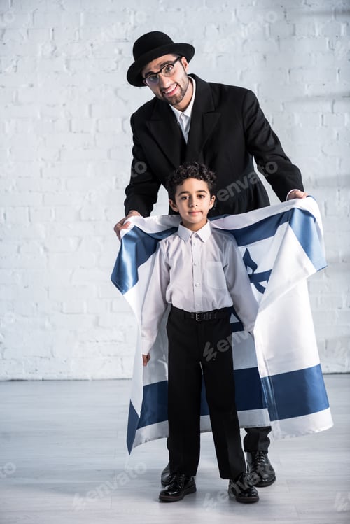 Preview: smiling jewish father holding flag of israel and cute son looking at camera