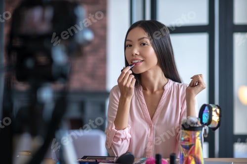 Preview: Appealing young woman coloring her lips while filming blog