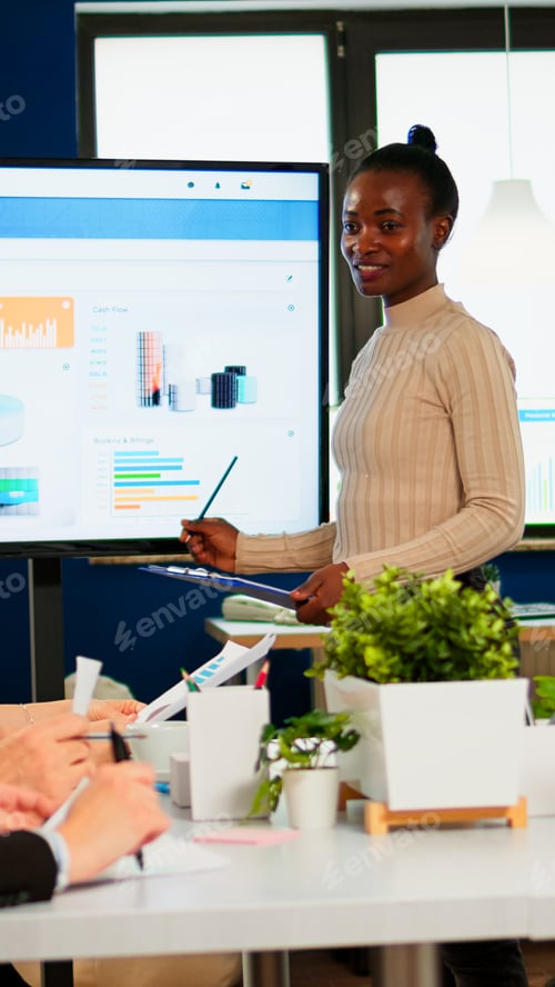 Preview: Black woman worker explaning company statistics in front of colleagues