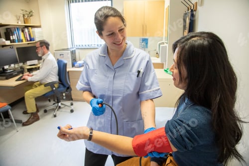 Preview: Nurse taking patient's blood pressure in a clinic, doctor in background