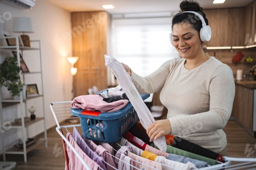 Preview: Woman listening to music while hanging the laundry on drying rack at home