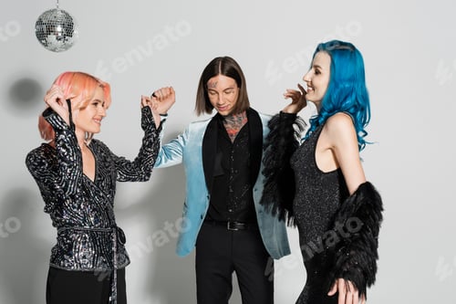 Preview: excited and stylish nonbinary people dancing near tattooed queer friend on grey background