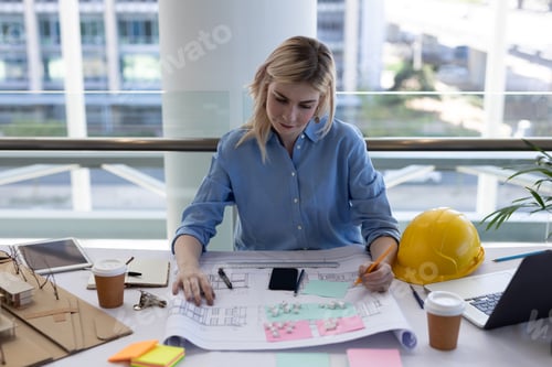 Preview: Front view of blonde young Caucasian female architect working at desk in modern office