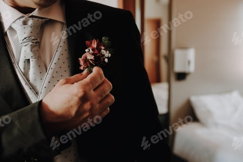 Preview: A groom places a floral pin on the lapel of his jacket, film grain added.