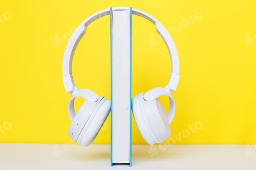 Aperçu: Audio book concept with white headphones and hardcover book on a yellow background.