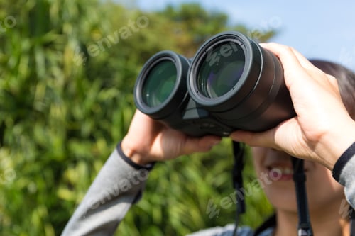 Preview: Young woman looking though binoculars at forest