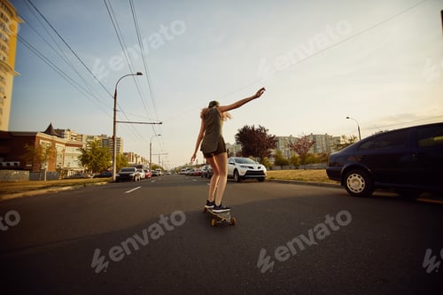 Preview: Beautiful young girl with tattoos riding longboard in sunny weather