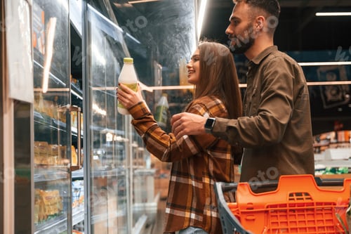 Preview: Side view, choosing products. Young couple are in supermarket together