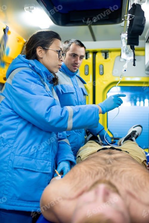 Preview: Two young paramedics preparing dropper for sick man inside ambulance car