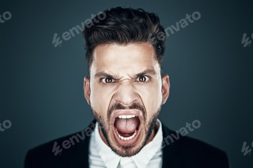 Preview: Angry young man making a face and looking at camera while standing against grey background