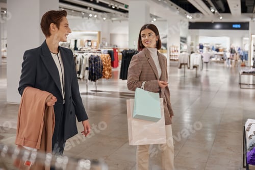 Preview: Happy young woman friends enjoying shopping together in big fashion shop mall