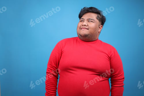 Preview: Smiling Young Asian Fat Male Looking to Aside Isolated on Blue Background