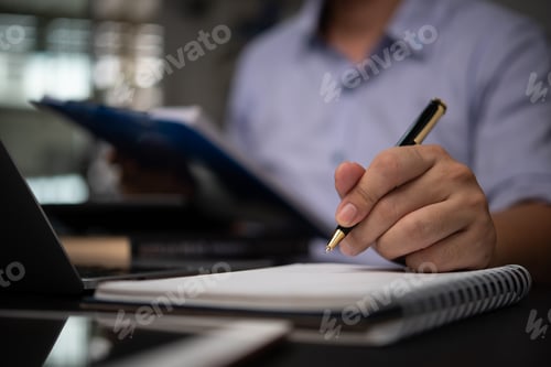 Preview: Business professional taking notes in a notebook while reviewing documents at a desk planning