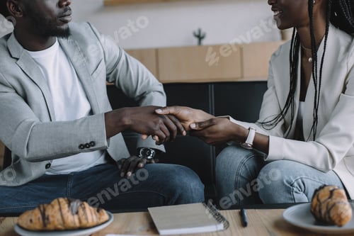 Preview: partial view of african american business partners shaking hands during business meeting in cafe