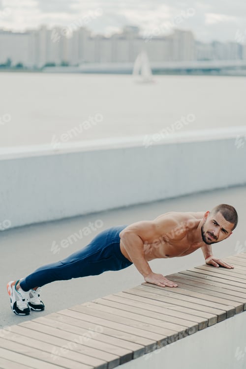 Preview: Flexible fit man does plank exercise on promenade has naked torso concentrated away p